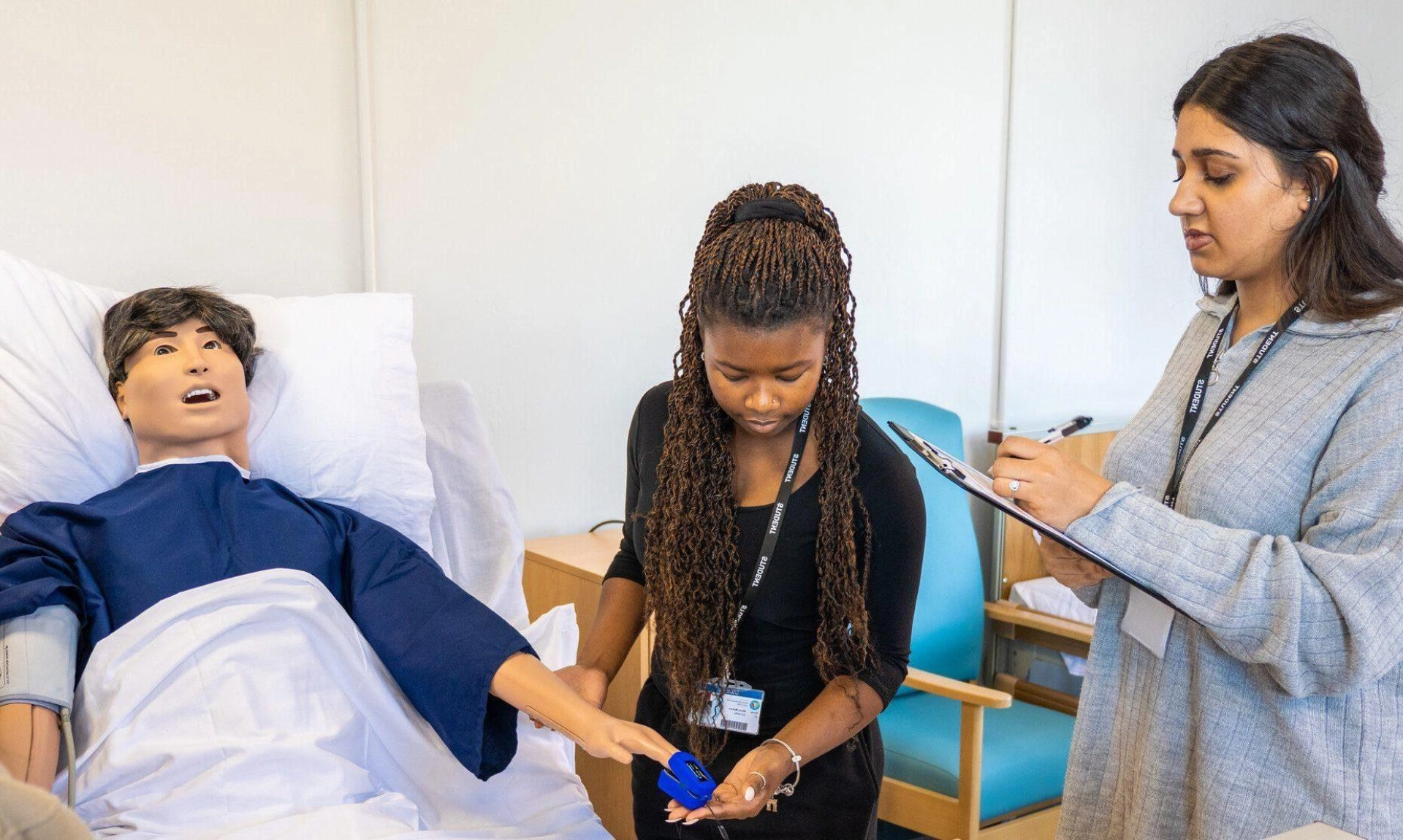 2 students around a medical bed treating a model patient