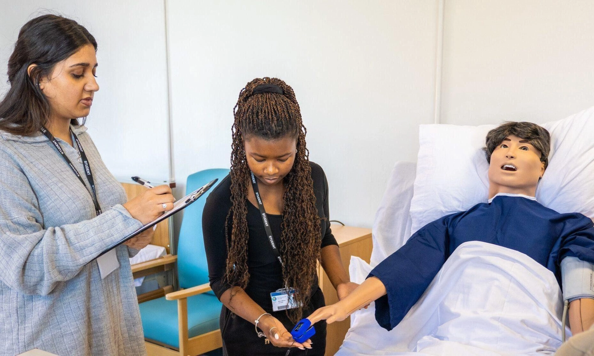 2 students on health course treating a model in a hospital bed