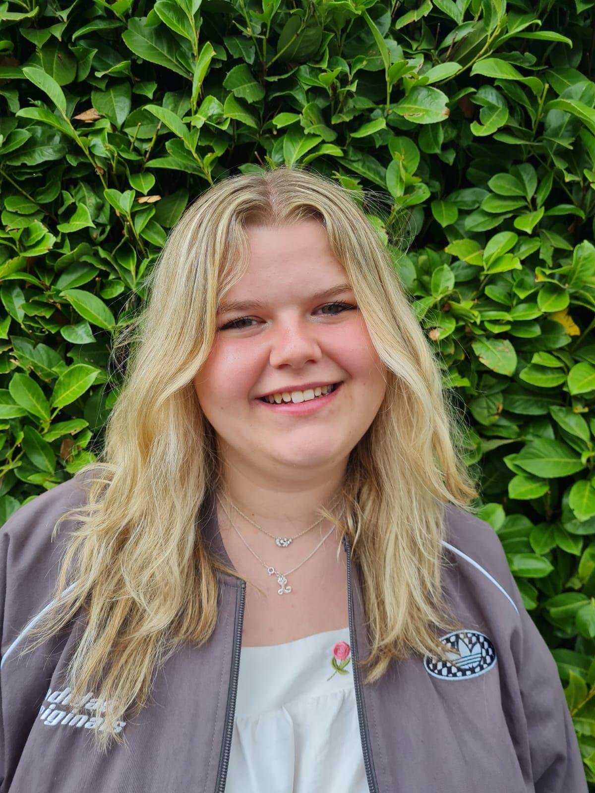 Picture of HoW College student Leonie smiling in front of a bush