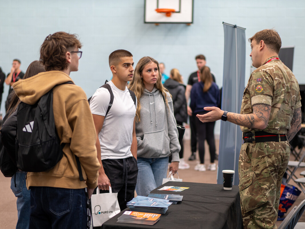 3 students speaking with a representative from the army at a careers fair in college