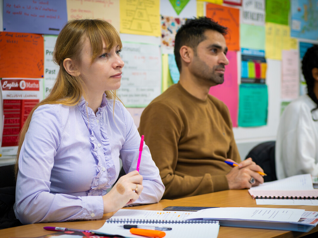 2 students sat in a classroom at a desk during a lesson listening to a teacher