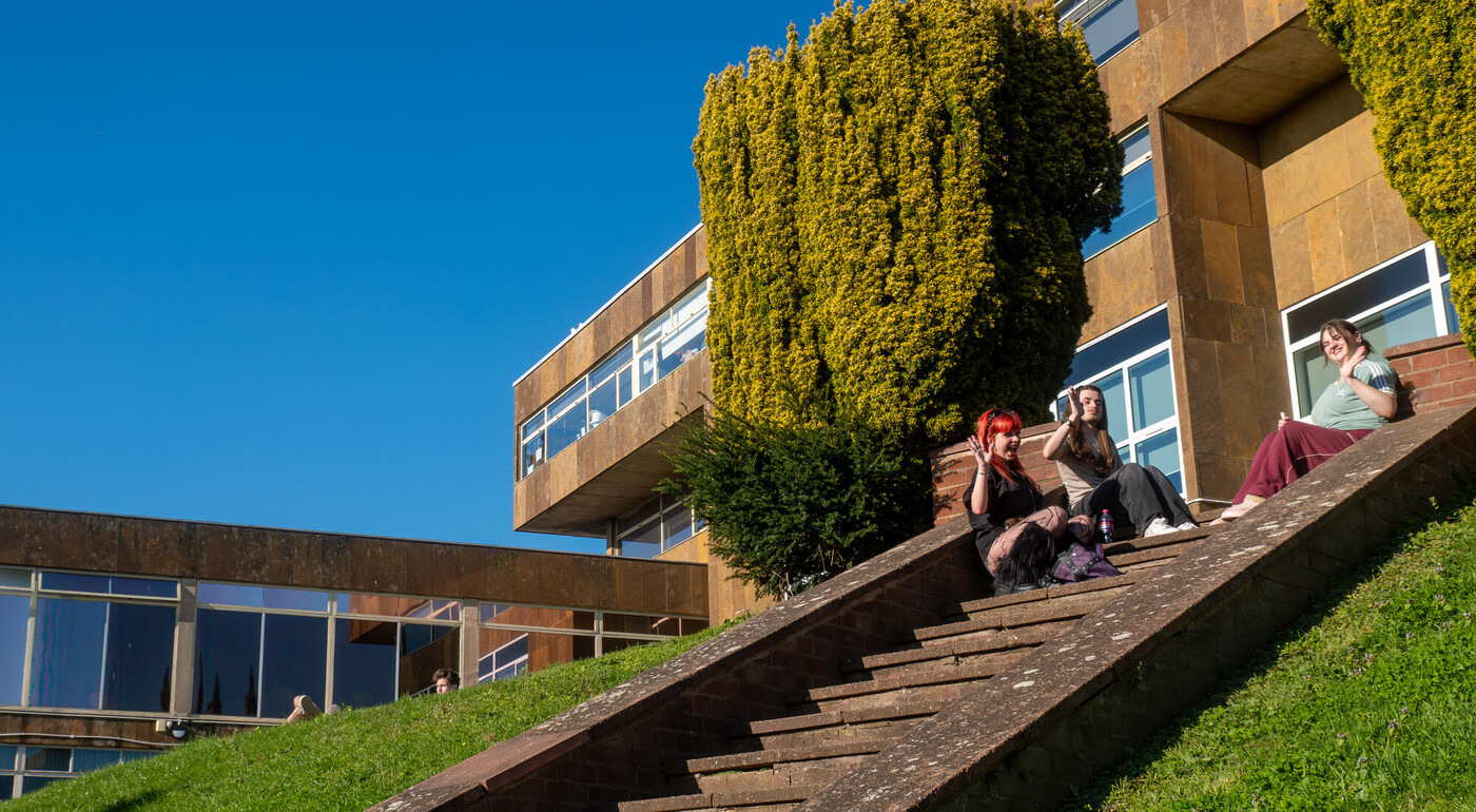 Picture of students sat in front of the All Saints campus waving in the sunshine