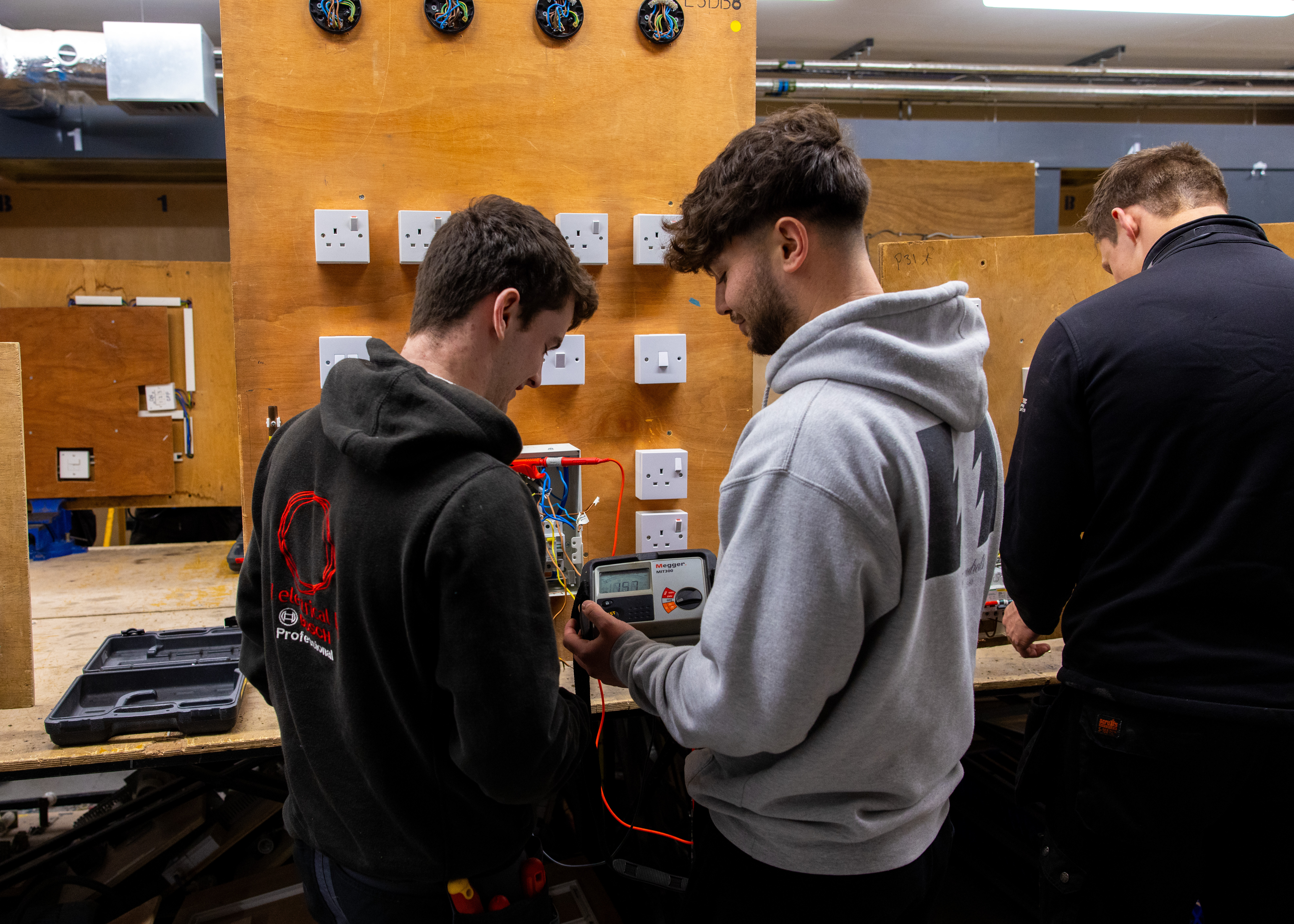 Three students working on switches and plugs in an electrical installation workshop
