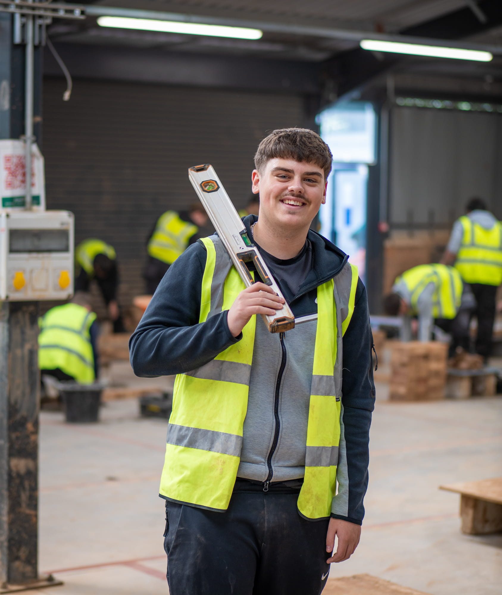 Student smiling in construction workshop holding a spirit level