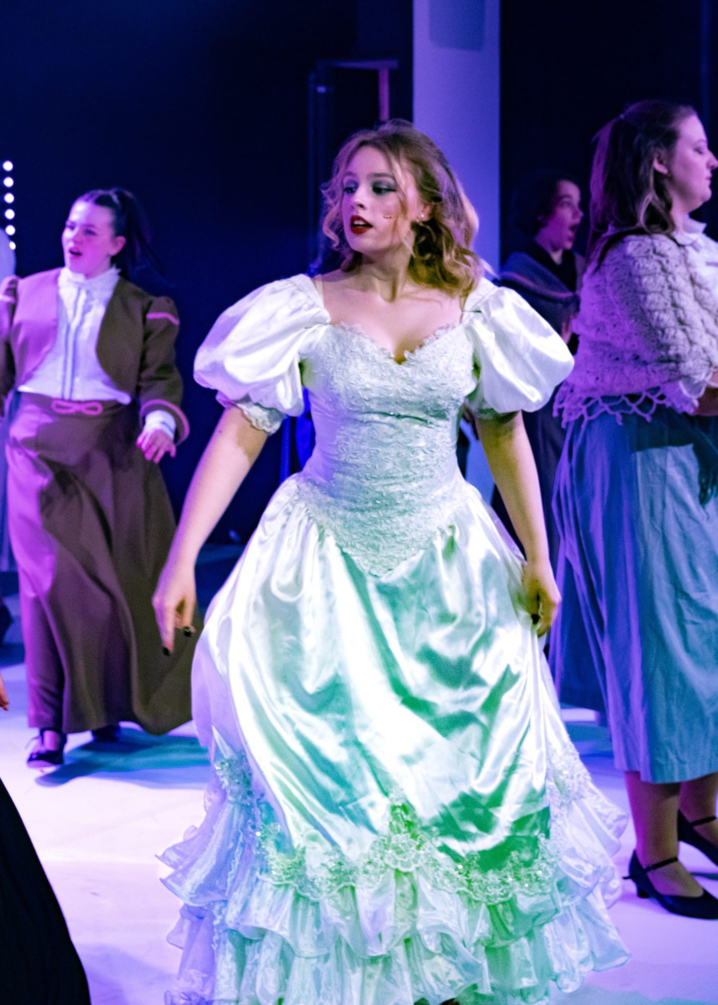 Student wearing a dress dancing on stage with other students behind her