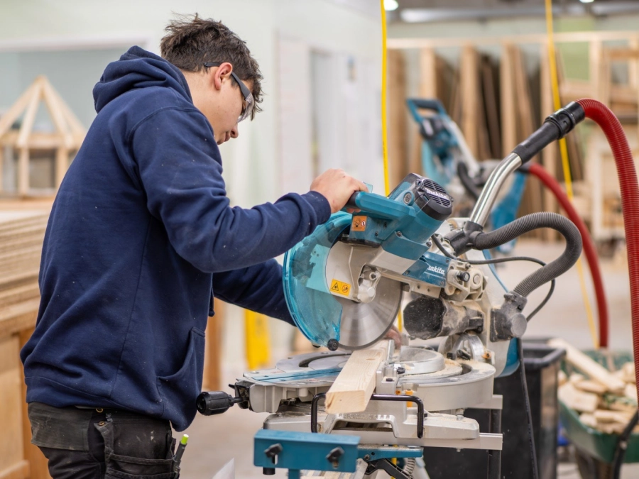 Apprentice using machinery cutting wood in a workshop