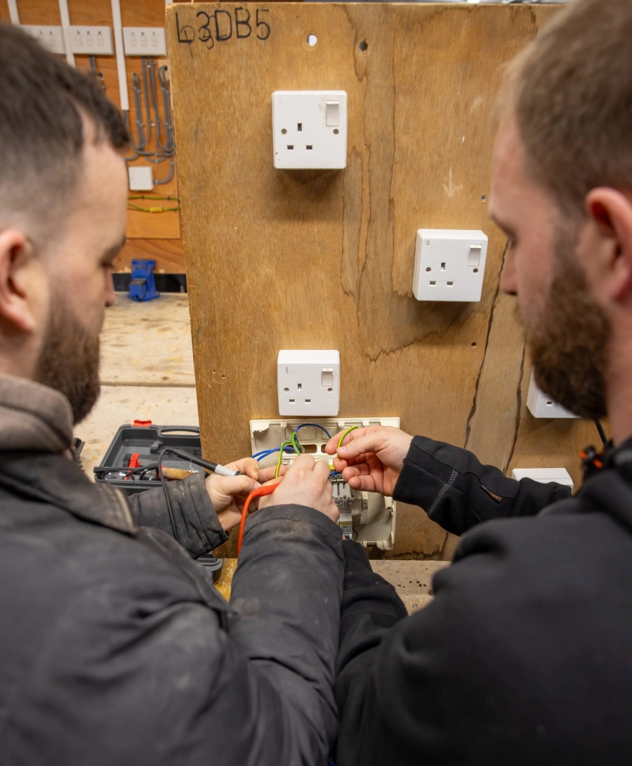 Two students helping each other wire a socket in a workshop