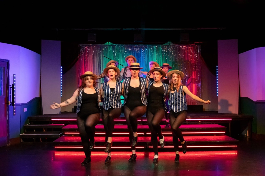 Five students stood centre stage dancing with their arms around each other