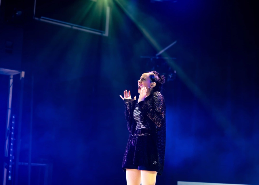 Student stood centre stage singing with lights around them