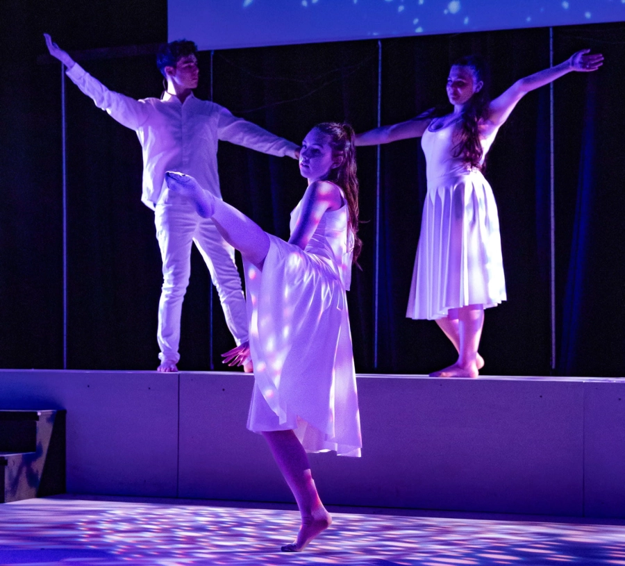 Three students dancing on stage wearing white