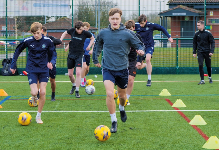 Students on a football pitch running with footballs
