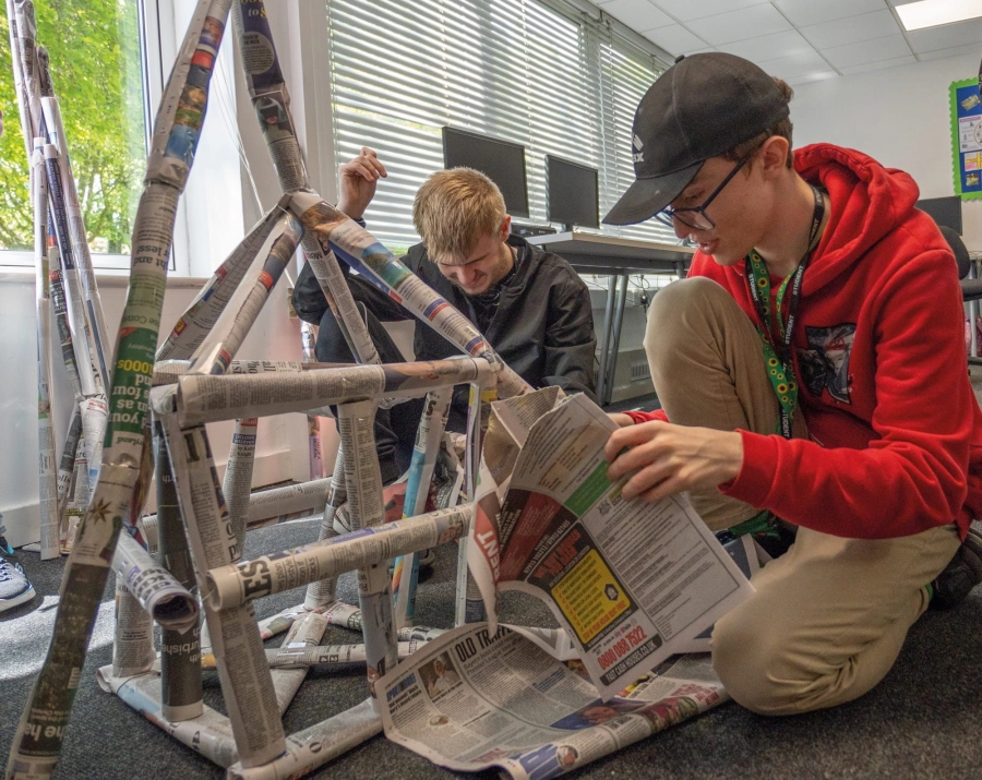 Two students knelt down building a tower out of newspape