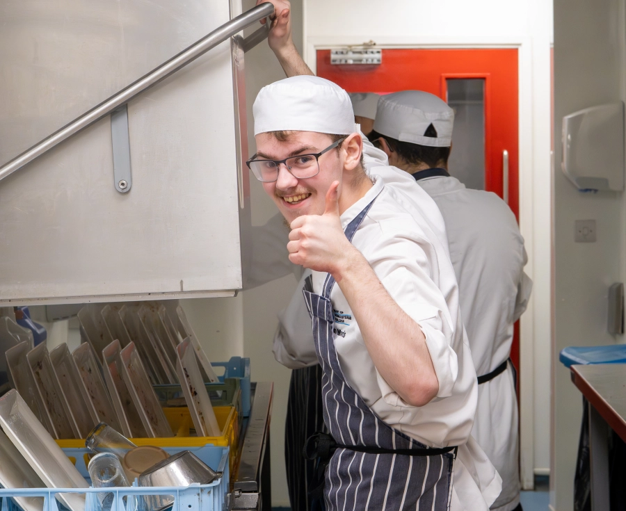 Student chef washing up in a kitchen putting their thumb up