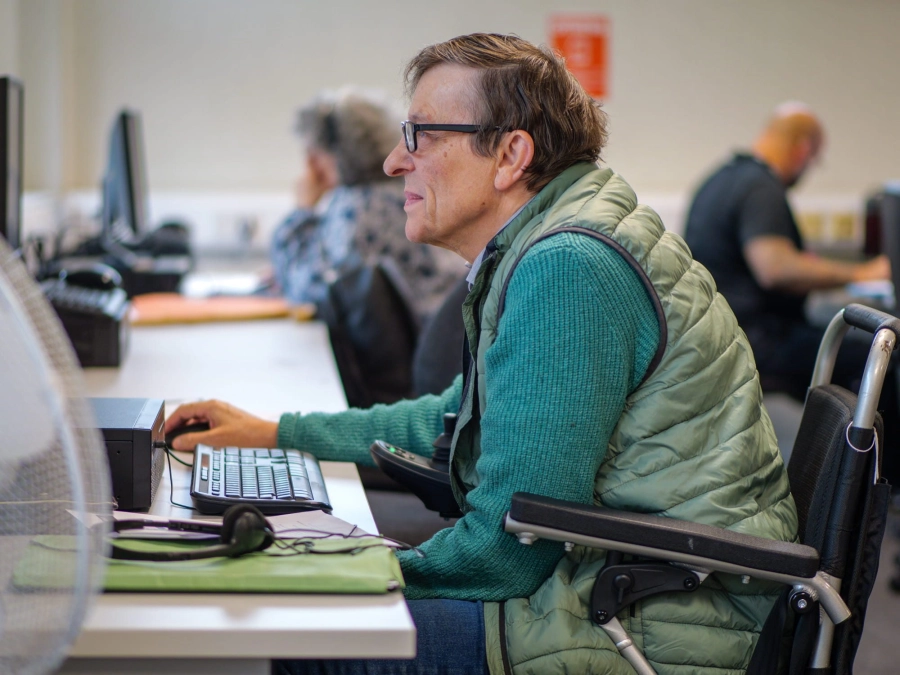 Adult learner in motorised chair working on a computer in a classroom