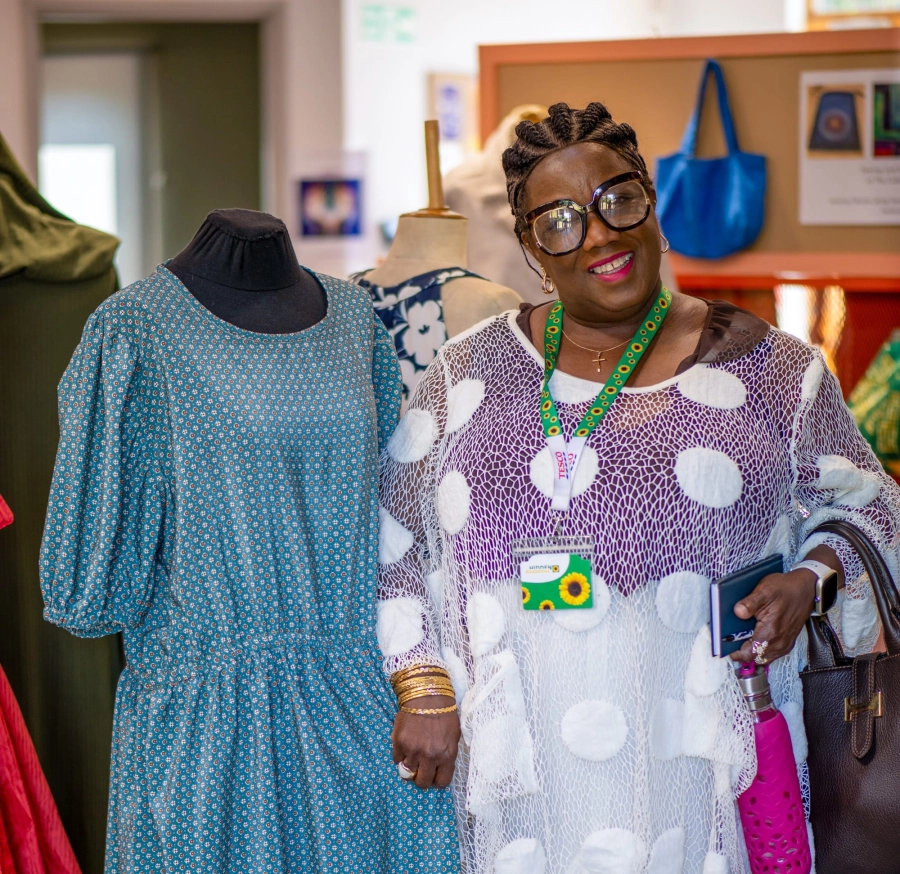 Adult learner smiling stood next to a blue dress in a sewing class