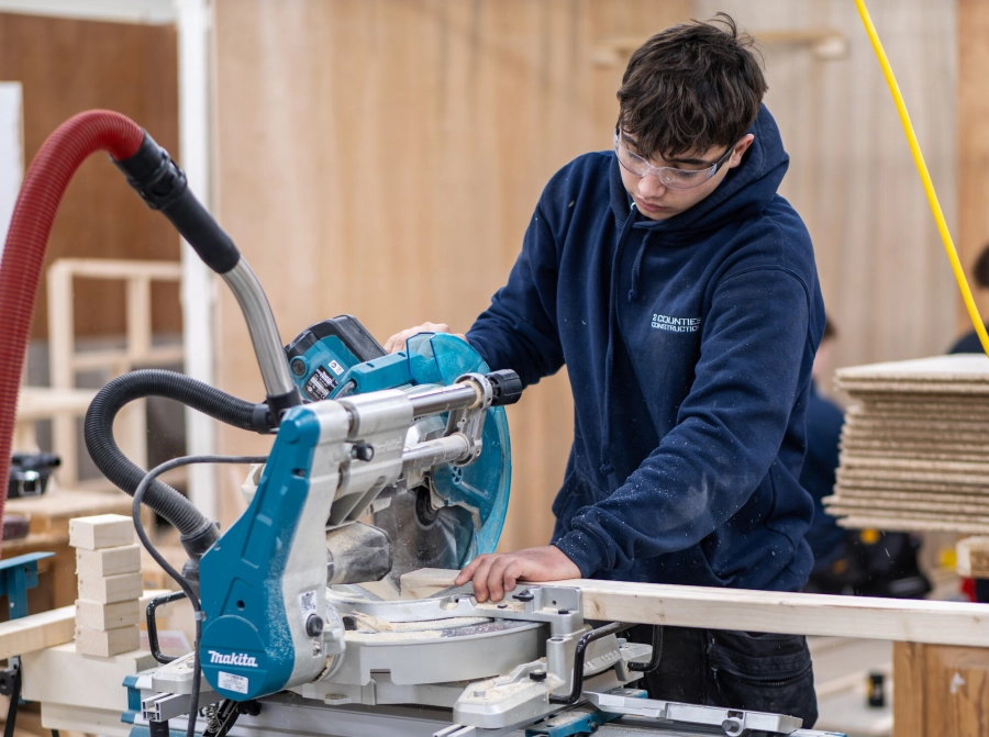 Student in a carpentry workshop using equipment to cut wood down