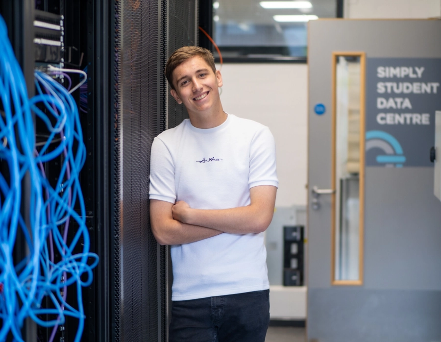 Student stood in front of IT equipment smiling and leaning