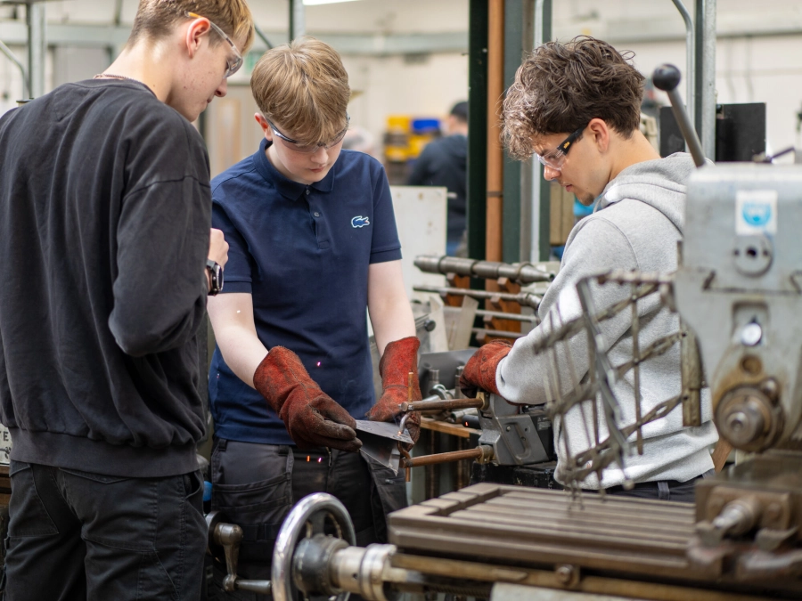 Three students wearing goggles working in a workshop with engineering equipment