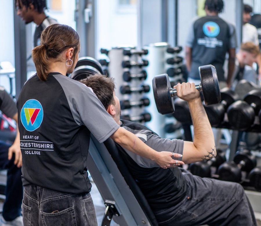 Student assisting another student with dumbells in the gym