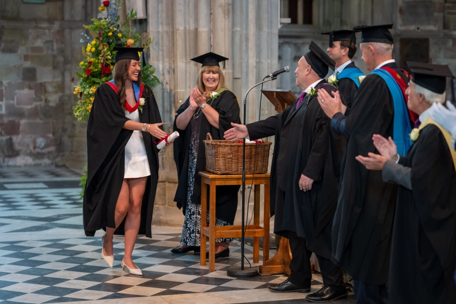 Student walking across cathedral shaking hands whilst collecting graduation certificate.