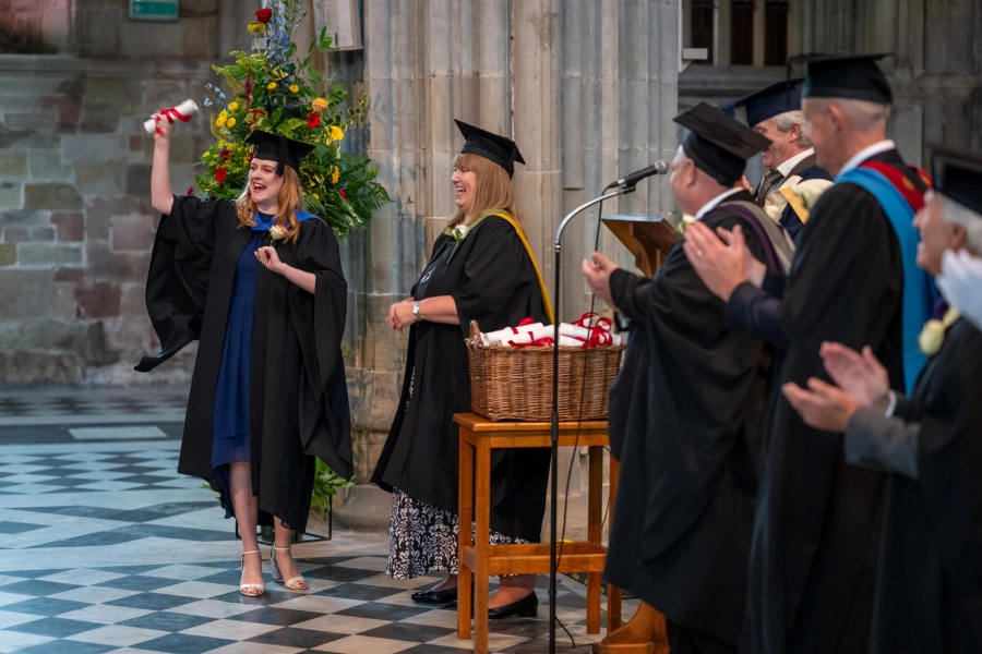 Student walking across the cathedral collecting her graduation certificate cheering and people clapping for her.