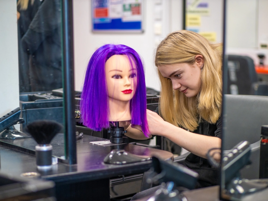 Hairdressing student working on a dolls head practicing hairdressing skills