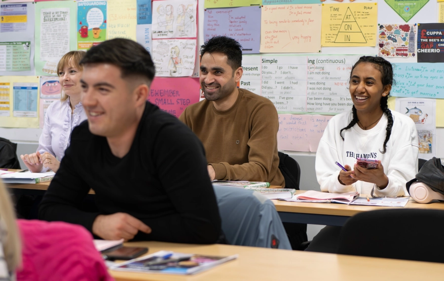 4 adult learners sat in a classroom smiling listening to their tutor.