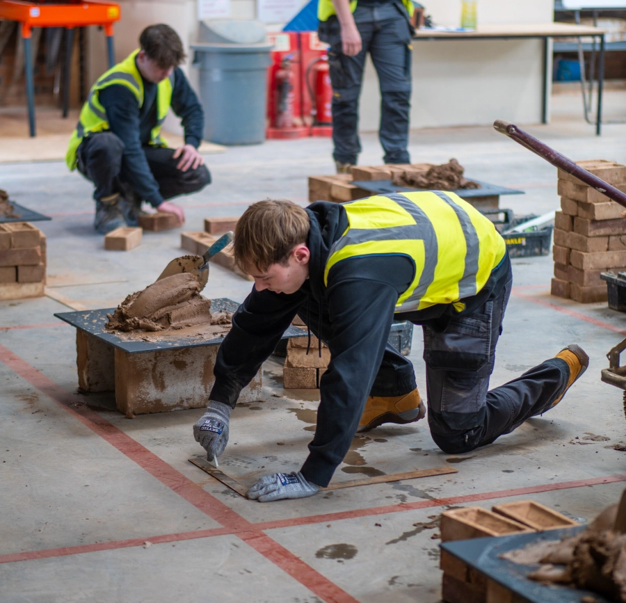 Two students knelt down doing bricklaying in the Colleges construction facilities