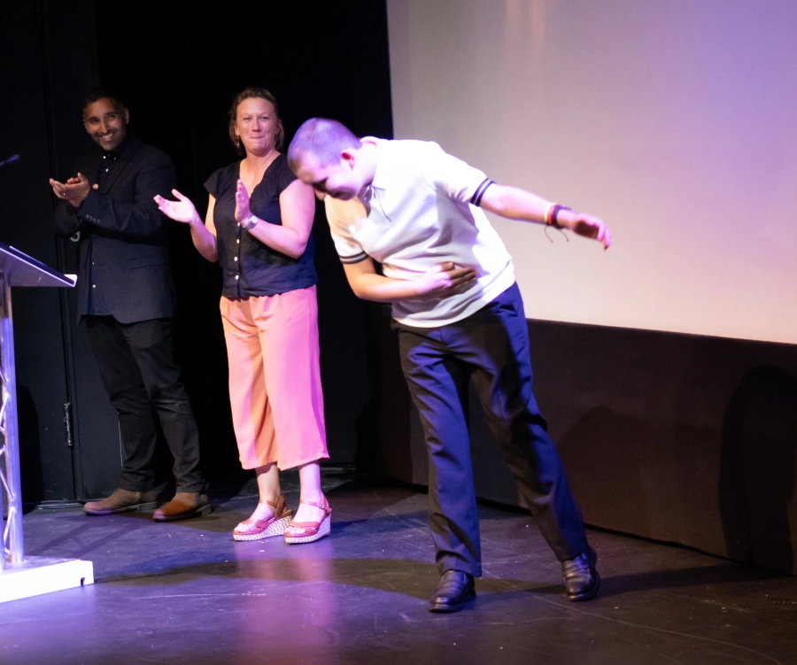 Student bowing on the stage stood by tutor and guest speaker