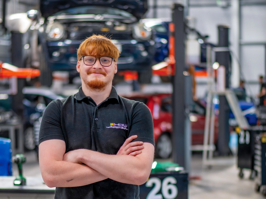Student standing in front of a car on a ramp in an automotive workshop
