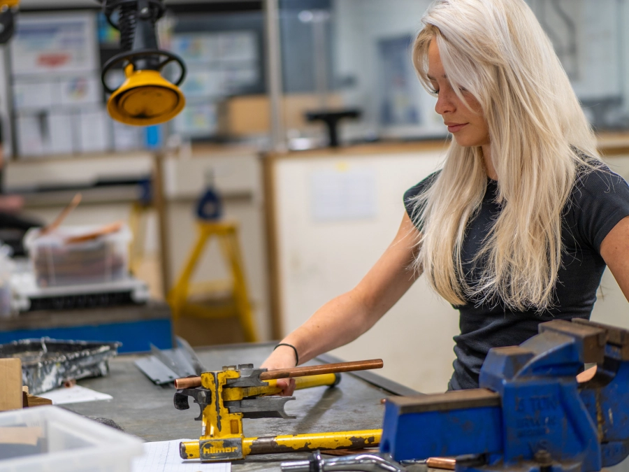 Female student working at a bench in an engineering workshop with tools and equipment.