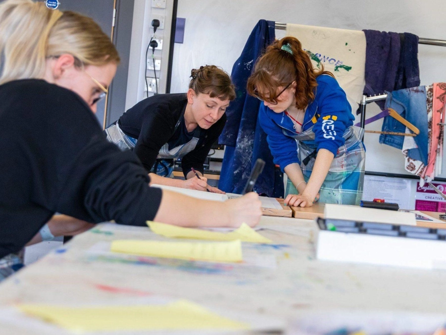 Group of students working on art around a table with their tutor in art workshops.