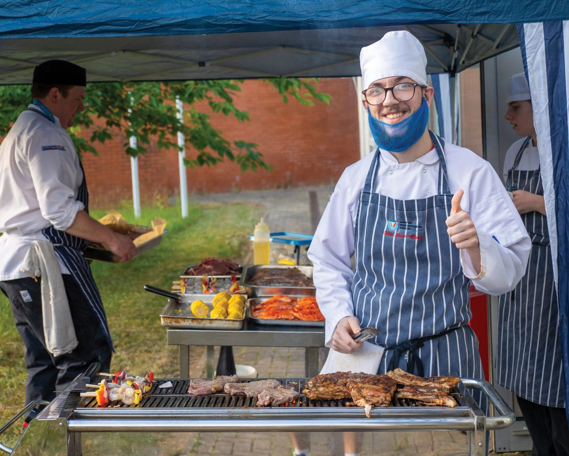 Student in chef whites smiling cooking bbq