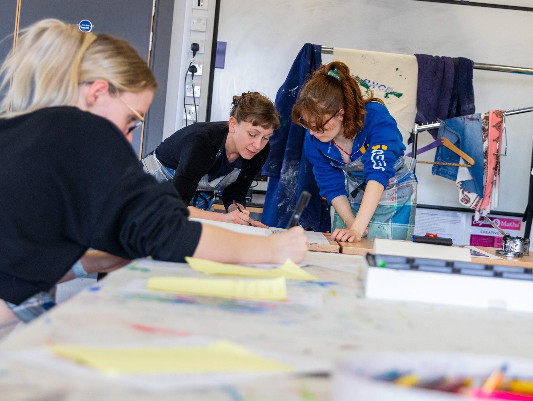 Two students with an art tutor completing work in an art studio classroom
