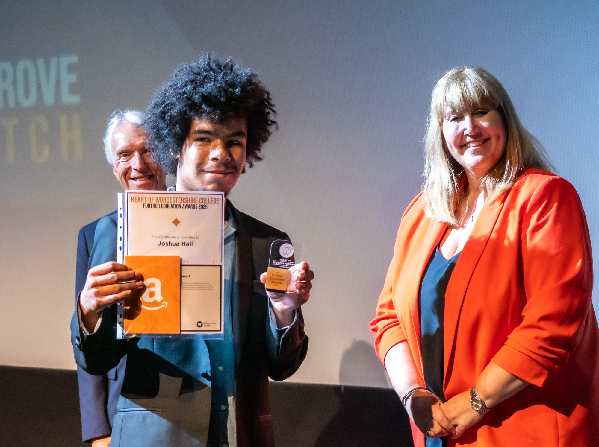 A picture of a student smiling with award and trophy at award ceremony with HoW College staff in the background